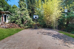 A gravel driveway leading to a basketball hoop in a wooded area with a small building on the left. - 4 BR home with foosball table, gym, and large yard (Indianola)