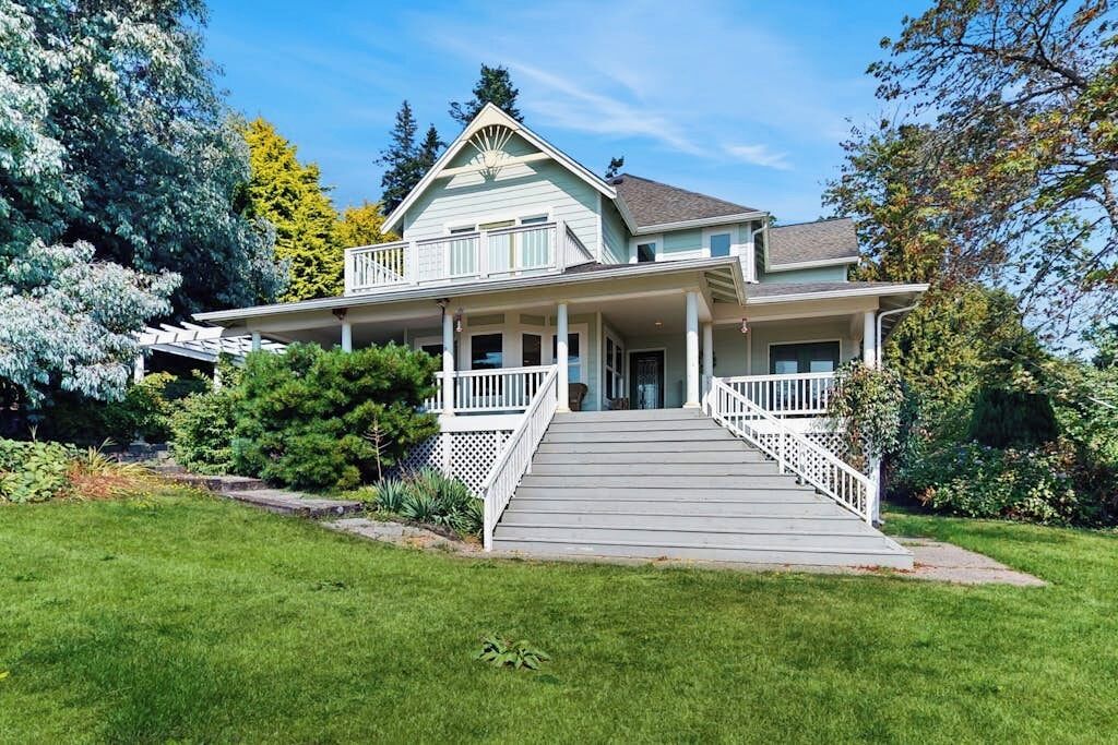 Ein zweistöckiges Haus mit Veranda, Treppe und gepflegtem Rasen.
