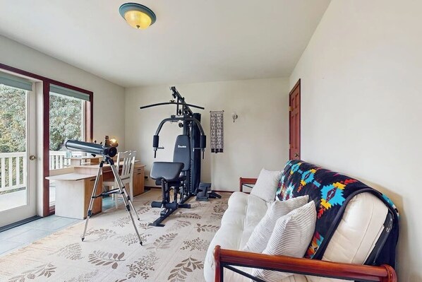 Una habitación con sofá, escritorio y silla, un telescopio y equipo de ejercicio.
