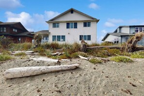A two-story building with a gabled roof, surrounded by natural vegetation and driftwood. - 3BR beachfront paradise with outstanding views (Sequim)