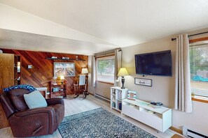 A living room with a brown leather sofa, a television mounted on the wall, and a wooden wall panel design. - Peaceful 3BR Oceanview Dog Friendly - Deck (Grayland)