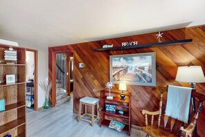 A room with wooden walls, a wooden floor, a desk with a lamp, a chair, a bookshelf, and a framed picture on the wall. - Peaceful 3BR Oceanview Dog Friendly - Deck (Grayland)