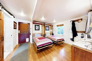 Une chambre avec deux lits, un plancher en bois, une porte avec une fenêtre et un petit bureau avec des papiers.