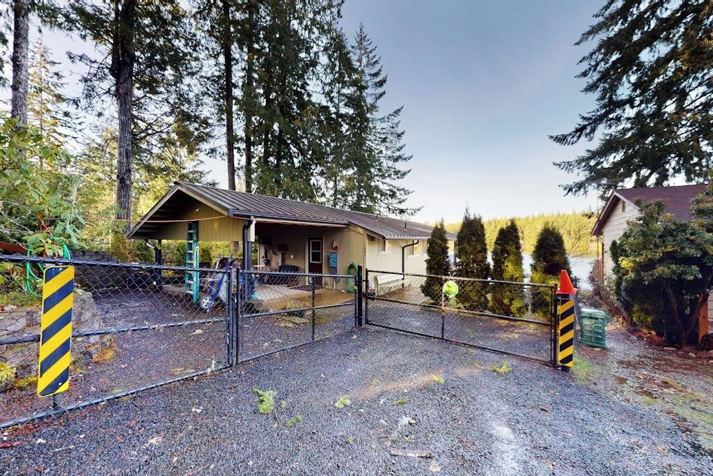 A fenced property with a small building, gravel ground, and tall trees in the background.