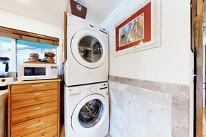 Un área de lavandería con lavadoras apiladas, un armario de madera y un cuadro en la pared.