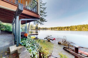 Une propriété au bord du lac, dotée d’une terrasse en bois, d’un quai et offrant une vue sur un lac paisible entouré d’arbres.