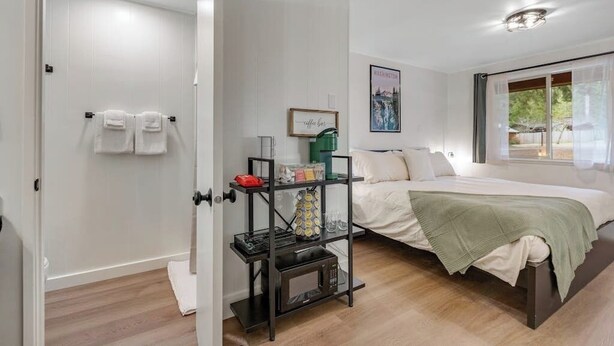 Une chambre à coucher avec un lit, une table de chevet, une étagère avec des objets et une fenêtre avec des rideaux.