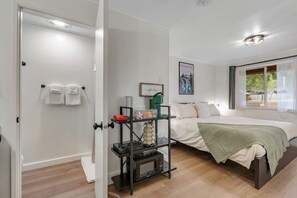 A bedroom with a bed, a bedside table, a shelf with items, and a window with curtains. - Lush 8BR mountain-view - fast WiFi, dog-friendly (Quilcene)