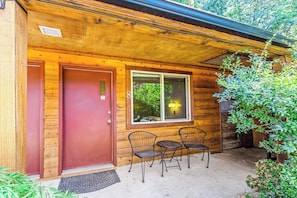 A wooden cabin with a red door, a window with a light fixture, and two metal chairs outside. - Lush 8BR mountain-view - fast WiFi, dog-friendly (Quilcene)