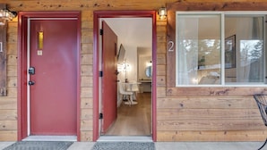 Une cabane en bois avec deux portes numérotées, un banc à l’extérieur et un intérieur visible avec une table et des chaises.