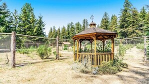 Un kiosque en bois surmonté d’une girouette, entouré d’une clôture et d’arbres.