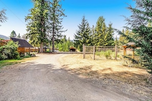 A rural road leading to a wooden cabin with a fenced yard and tall trees. - Lush 8BR mountain-view - fast WiFi, dog-friendly (Quilcene)