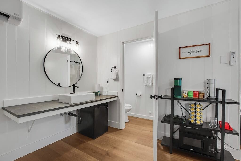 Une salle de bain moderne avec un miroir rond, un lavabo blanc et un coin café.