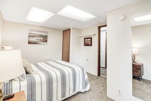 Une chambre à coucher avec un lit, une table de chevet, une lampe, un tableau accroché au mur et une porte donnant sur une autre pièce.