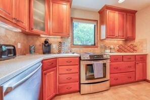 A kitchen with wooden cabinets, a stainless steel oven, and a window with a view of trees. - Incredible 3BR Bayview Dog Friendly - Dock (Gig Harbor)