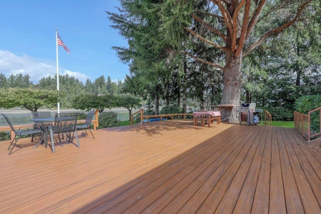 Una terraza de madera con mobiliario exterior, una bandera y un árbol grande.