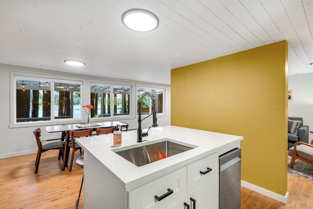 A modern kitchen with a white countertop, a built-in dishwasher, and a window overlooking a garden.
