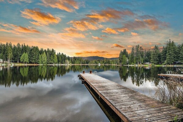 A wooden dock extending into a calm lake with a forested shoreline and a sunset in the background. - Skiing 1BR Lakefront - Dock - Deck - Firepit (Fall City)