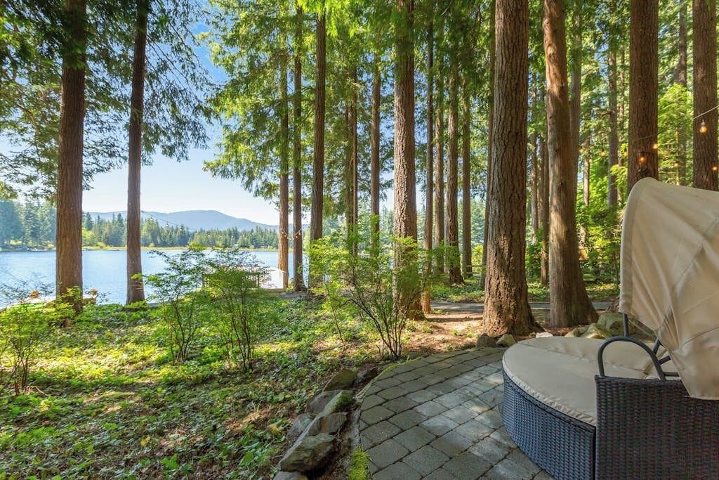 Eine Terrassenfläche mit einem Rattansofa und Blick auf einen See, der von hohen Bäumen umgeben ist.