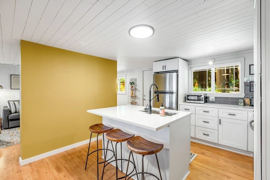Una cocina moderna con una isla central, taburetes de bar y muebles de cocina blancos.
