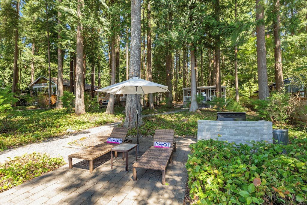 A wooden deck with lounge chairs and a table, surrounded by a forested area.