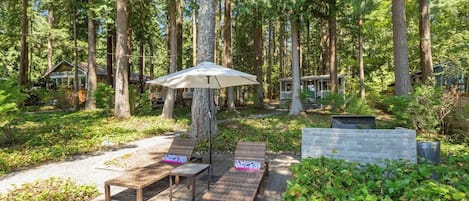 A wooden deck with lounge chairs and a table, surrounded by a forested area.