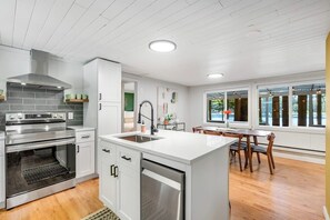 A modern kitchen with a built-in oven, a dishwasher, and a dining area with a table and chairs. - Skiing 1BR Lakefront | Dock | Deck | Firepit (Fall City)