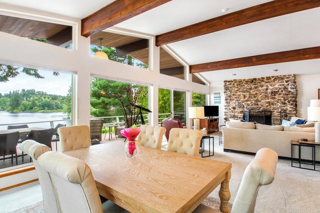 Un amplio salón con una mesa de comedor de madera, asientos cómodos, una chimenea de piedra y grandes ventanales con vistas al exterior.