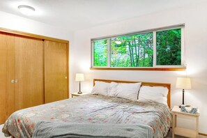 A bedroom with a bed, two bedside tables, a window with a view of trees, and a wardrobe. - 4BR Lakefront - Dock - Fireplace - Balcony (Olympia)