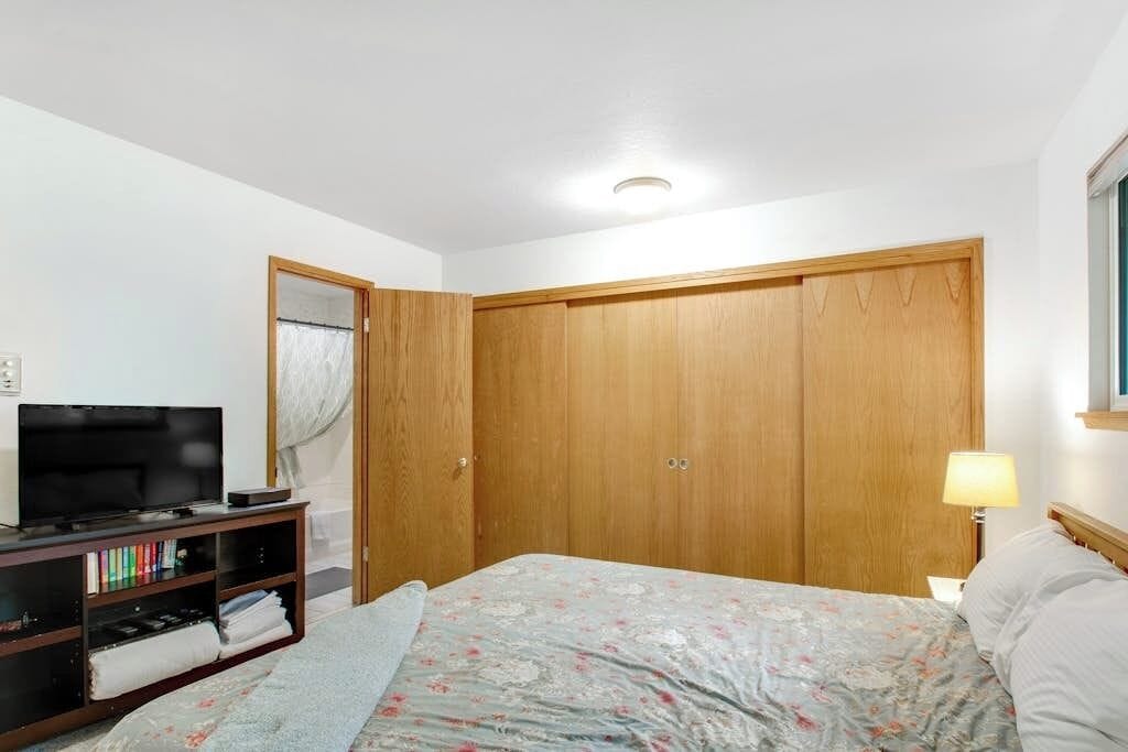 A bedroom with a bed, a TV on a stand, a wardrobe, and a bedside lamp.