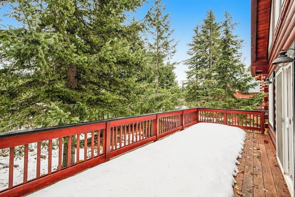 Een sneeuwbedekt terras met een rode balustrade, omringd door hoge altijdgroene bomen.