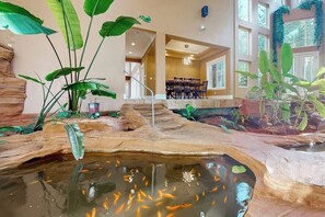 A room with a koi pond, indoor plants, and a dining area with chairs.