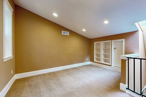 A room with beige carpet, white trim, recessed ceiling lights, and a white door with a glass panel.