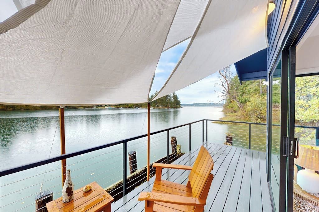 A deck with wooden chairs and a table, overlooking a calm body of water and greenery.