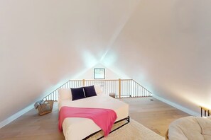Un dormitorio con cama, piso de madera, barandal blanco y un cuadro en la pared.