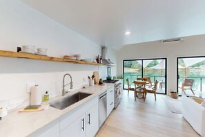 Una cocina moderna con un amplio ventanal, estantes de madera y una zona de comedor con sillas.