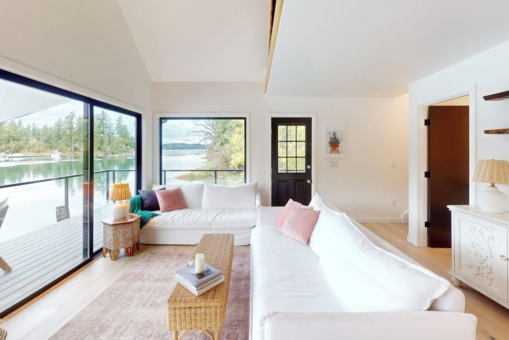 A modern living room with a large window, a white sofa, a small side table, and a view of a lake.