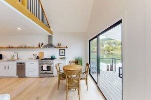 Una cocina moderna con comedor, un amplio ventanal con vistas a un lago y una terraza de madera.