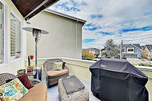 Eine Terrassengruppe mit Korbmöbeln, einem Grill und Blick auf benachbarte Häuser.