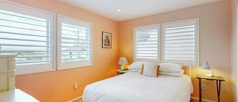A bedroom with a bed, two bedside tables, and a window with blinds.
