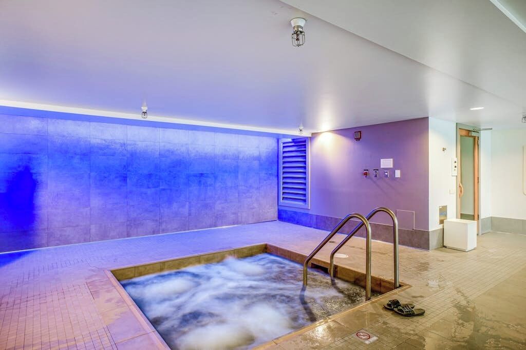 A spa area with a hot tub, a shower, and a window with blinds.