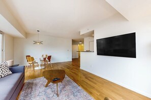 A modern living room with a sofa, coffee table, and chairs, a flat-screen TV mounted on the wall, and a wooden floor. - Downtown condo with city views, pool (Seattle)