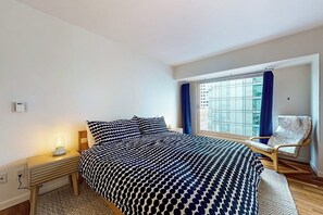 Ein Schlafzimmer mit einem Bett, einem Sessel, einem Nachttisch und einem Fenster mit Vorhängen.