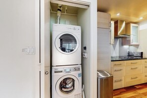 Eine kleine Küche mit integrierter Waschmaschine und Trockner, Holzschränken und einem Edelstahlkühlschrank.