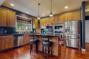A modern kitchen with wooden cabinets, stainless steel appliances, and a central island with bar stools. - 4BR Enumclaw home-AC-grill-fireplace-walk to town (Enumclaw)