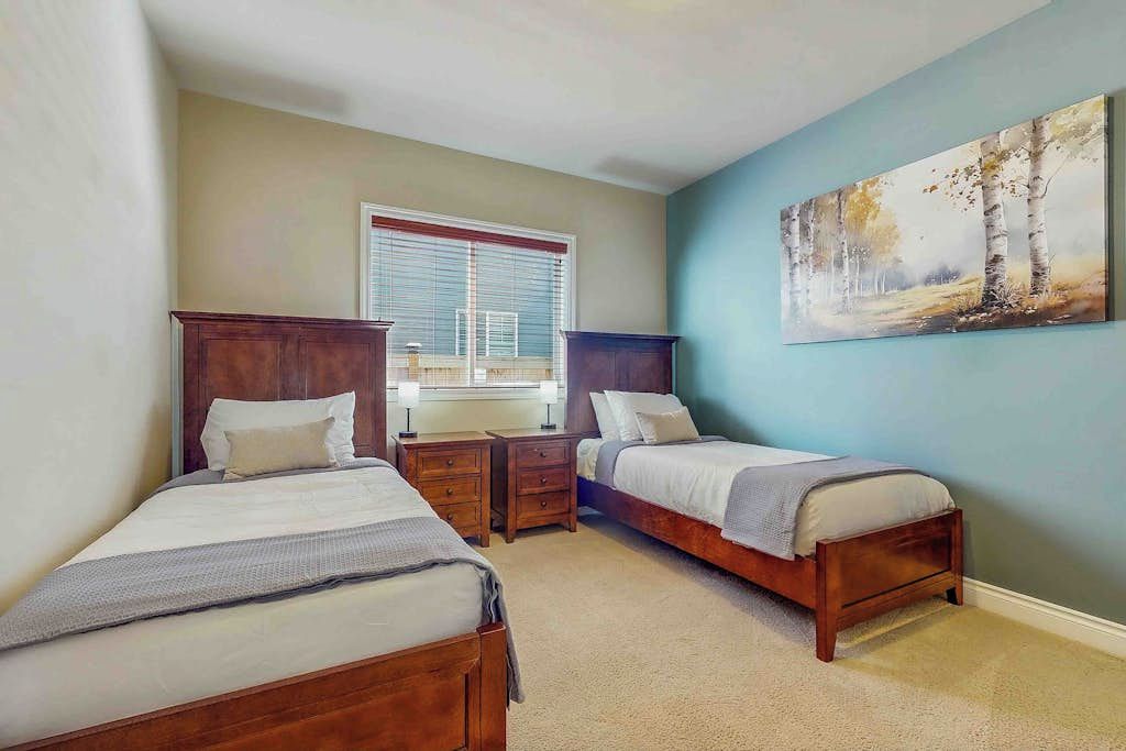 A bedroom with two beds, a window with blinds, and a painting on the wall.