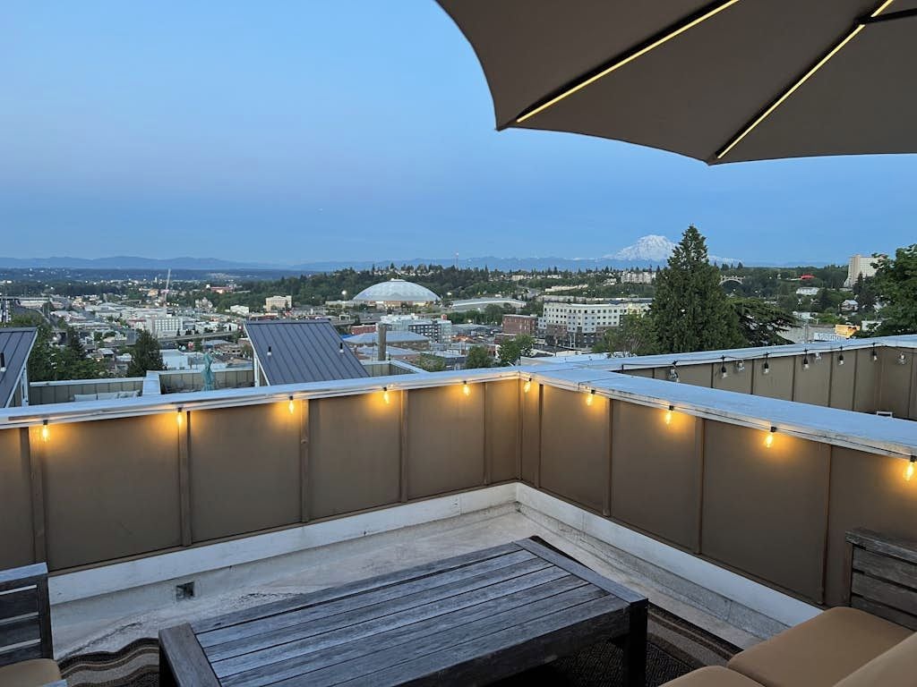 A rooftop terrace with a view of a cityscape, including buildings and a mountain.