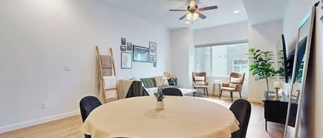 A dining area with a round table, chairs, ceiling fan, and wall-mounted TV.