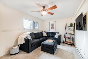A living room with a sectional sofa, a ceiling fan, a bookshelf, and a window. - Comfortable 3BR - Deck - Washer Dryer (University Place)