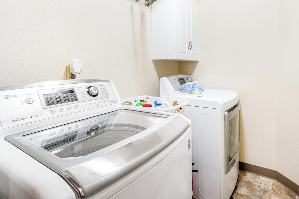 A laundry area with a front-loading washer and dryer, a control panel, and a cabinet above the dryer.